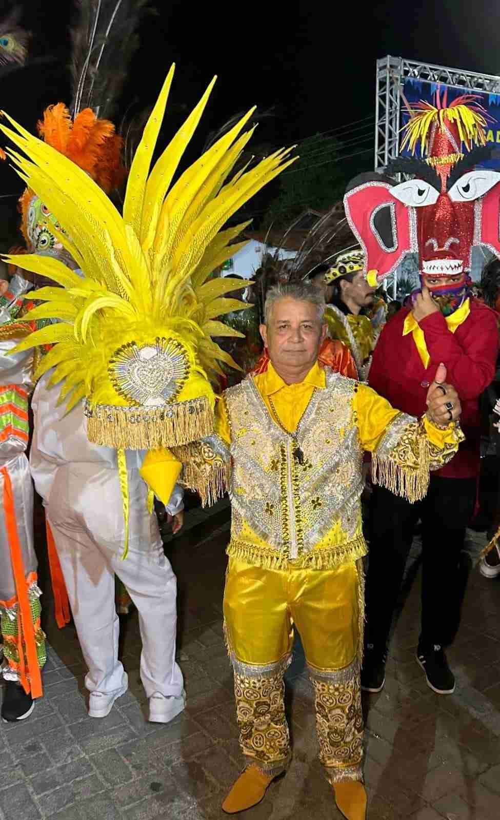 Dois participantes com trajes festivos, um segurando adereÃ§o amarelo