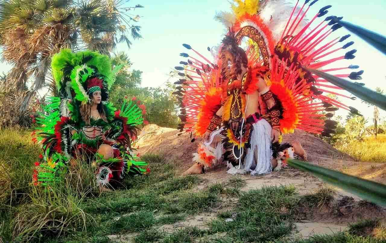 Two performers in vibrant red and green feathered costumes posing outdoors